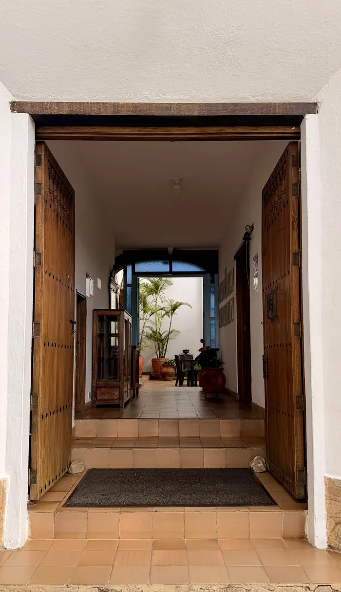 Entrada principal de la posada: portón de madera abierto hacia un corredor que lleva al patio