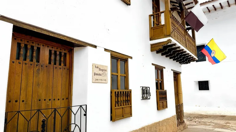 Fachada blanca de la posada con portón de madera, ventanas con balaústres, balcón de madera y el letrero Los Ángeles Posada