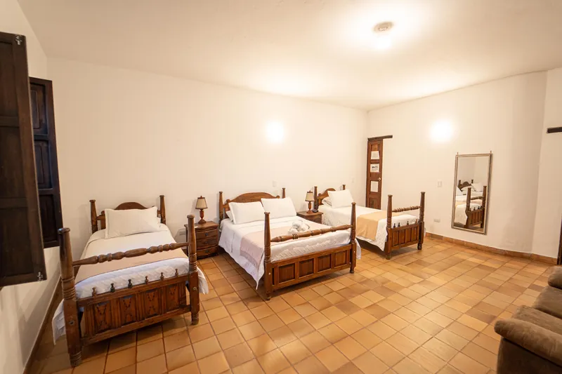 Habitación San Antonio con tres camas de madera tallada, espejo y luz cálida