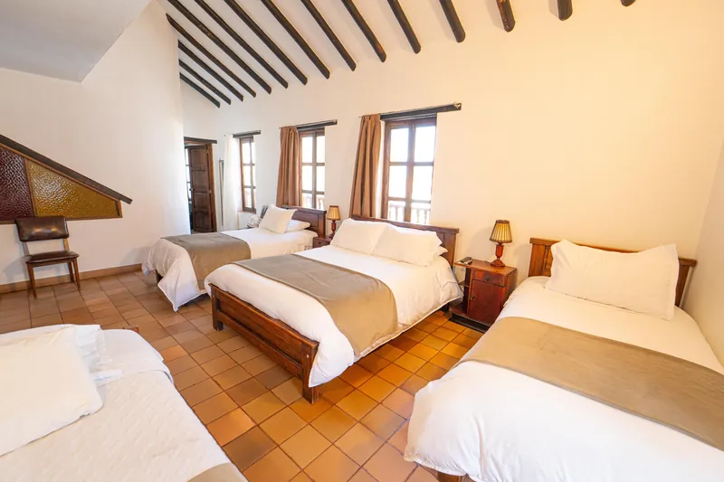 Habitación San Gabriel con cuatro camas, techo alto de vigas y ventanas al balcón