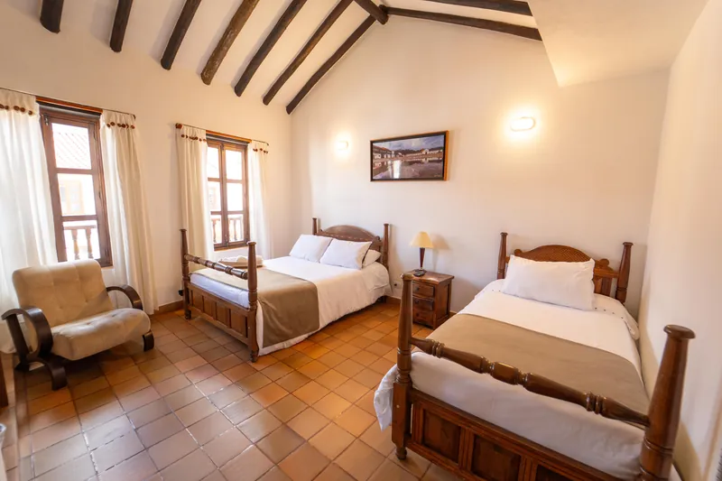 Habitación San José con cama doble, cama sencilla, sillón y ventanas con balcón