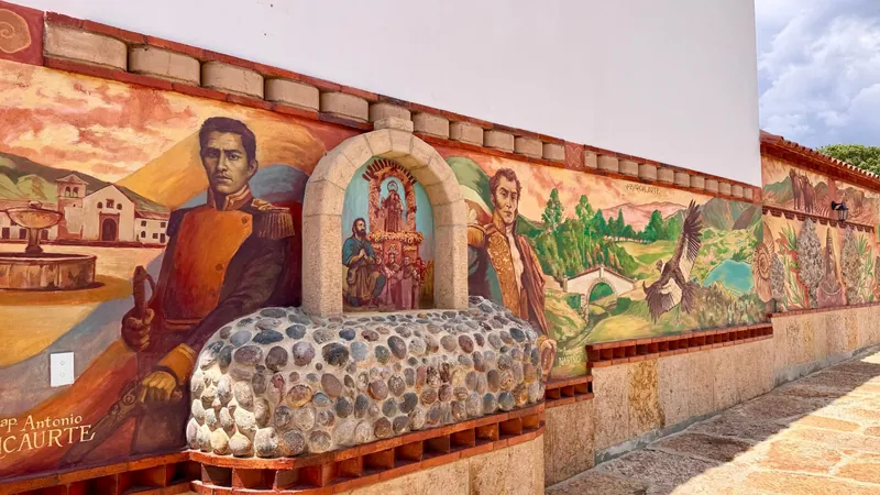 Murales en el muro del parqueadero con Antonio Ricaurte, Antonio Nariño, un cóndor y paisajes de Boyacá, junto a un nicho de piedra