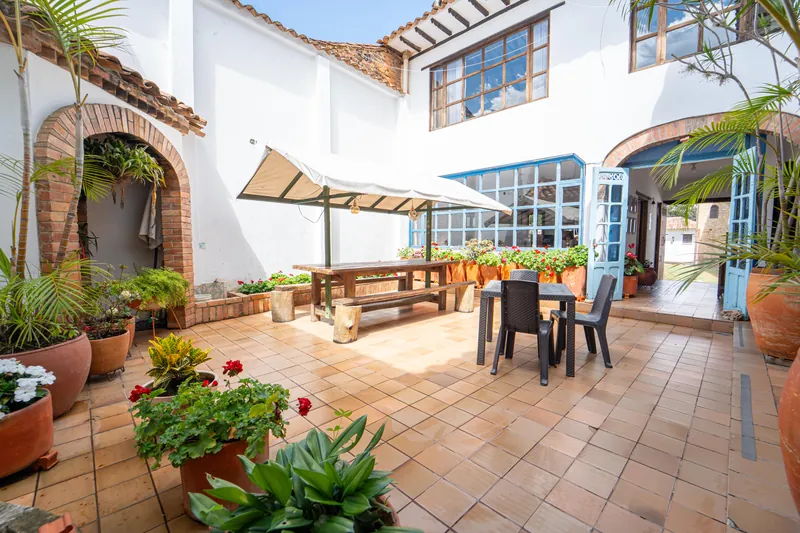 Patio interior con mesas de madera, toldo blanco y ventanas de marco azul